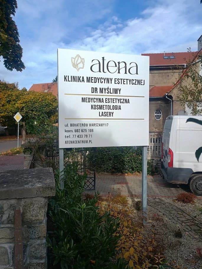 Jasny szyld Atena na dwóch podporach przed posesją, z nazwą kliniki i listą usług