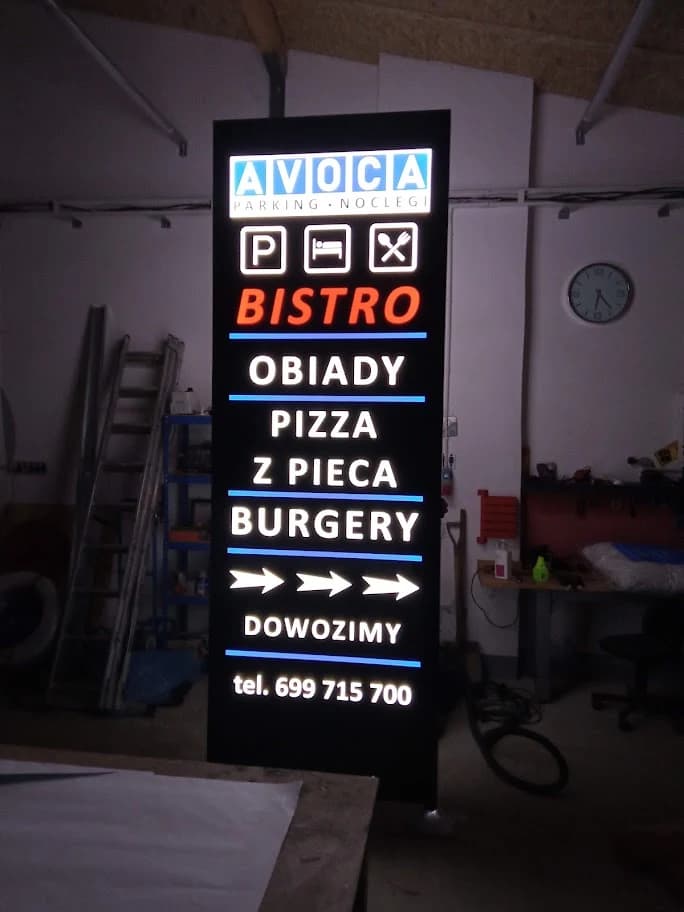 Włączony pylon AVOCA Bistro w warsztacie, z białymi napisami, pomarańczowym BISTRO i niebieskimi liniami