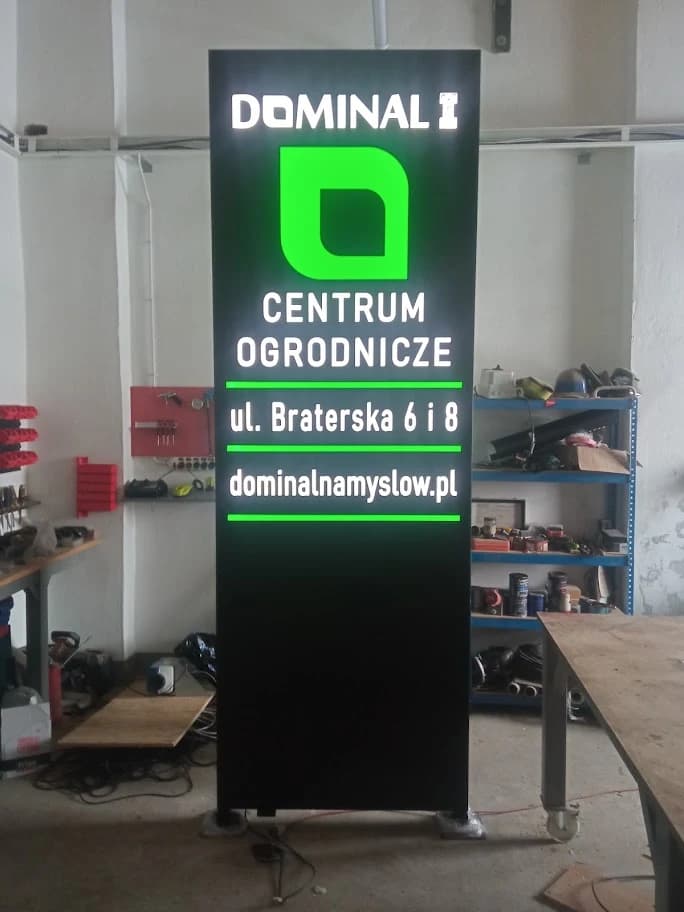 Pylon Dominal w warsztacie z podświetlonym zielonym logo i białymi napisami na czarnym tle