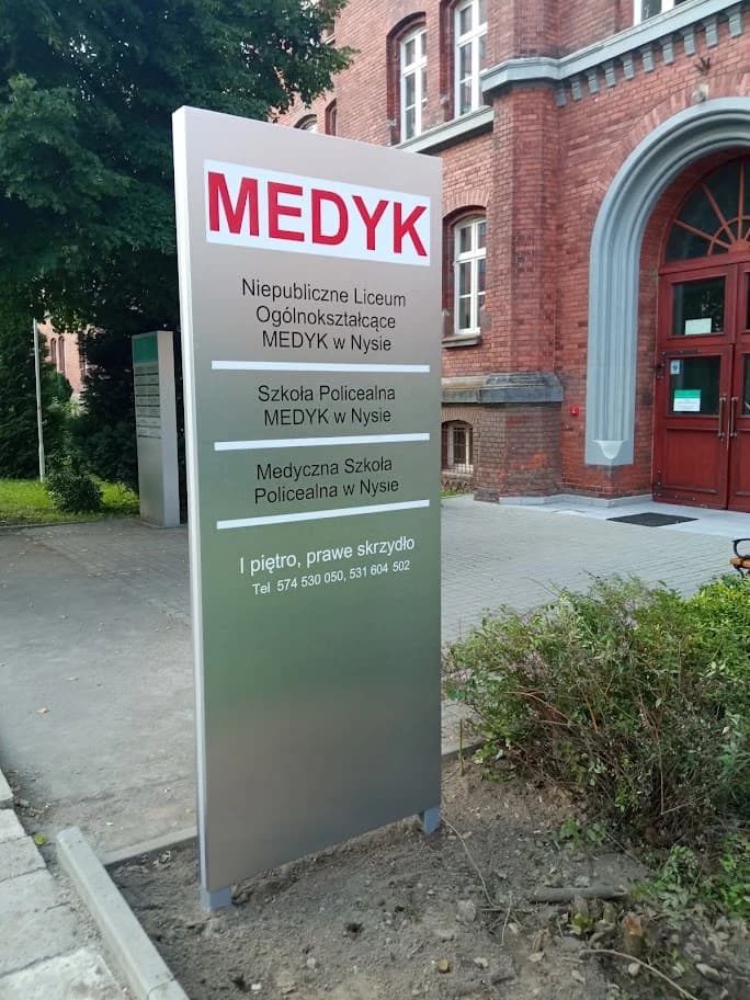 Srebrzysty pylon MEDYK obok wejścia do ceglanego budynku szkoły w Nysie